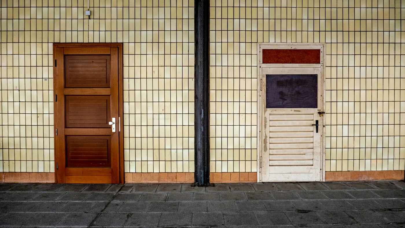 Two different doors set into a tiled wall, one dark timber and one white with louvres