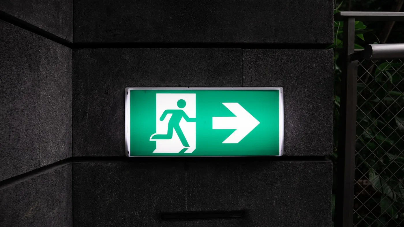 An illuminated green exit sign on a dark concrete wall