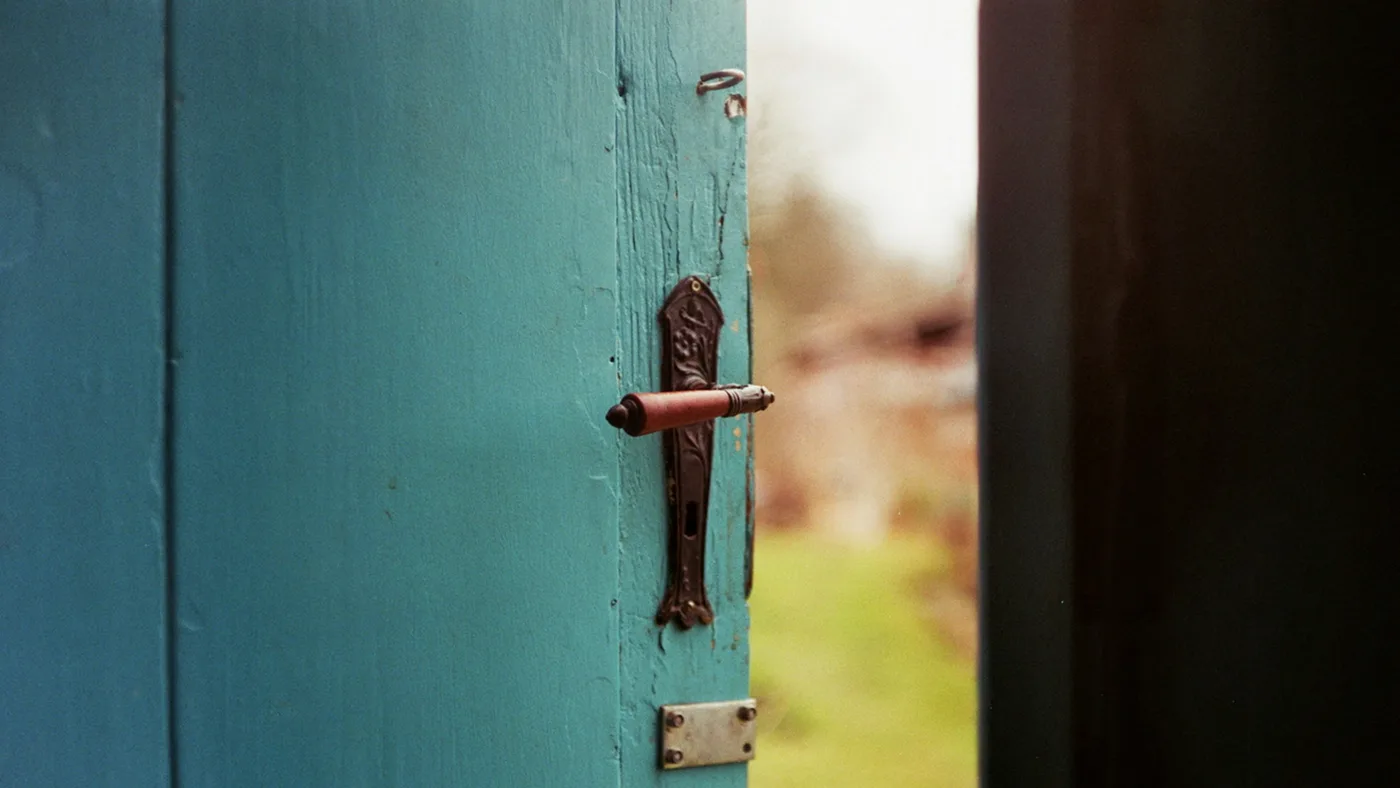 A weathered turquoise wooden door standing half open onto a soft, blurred garden