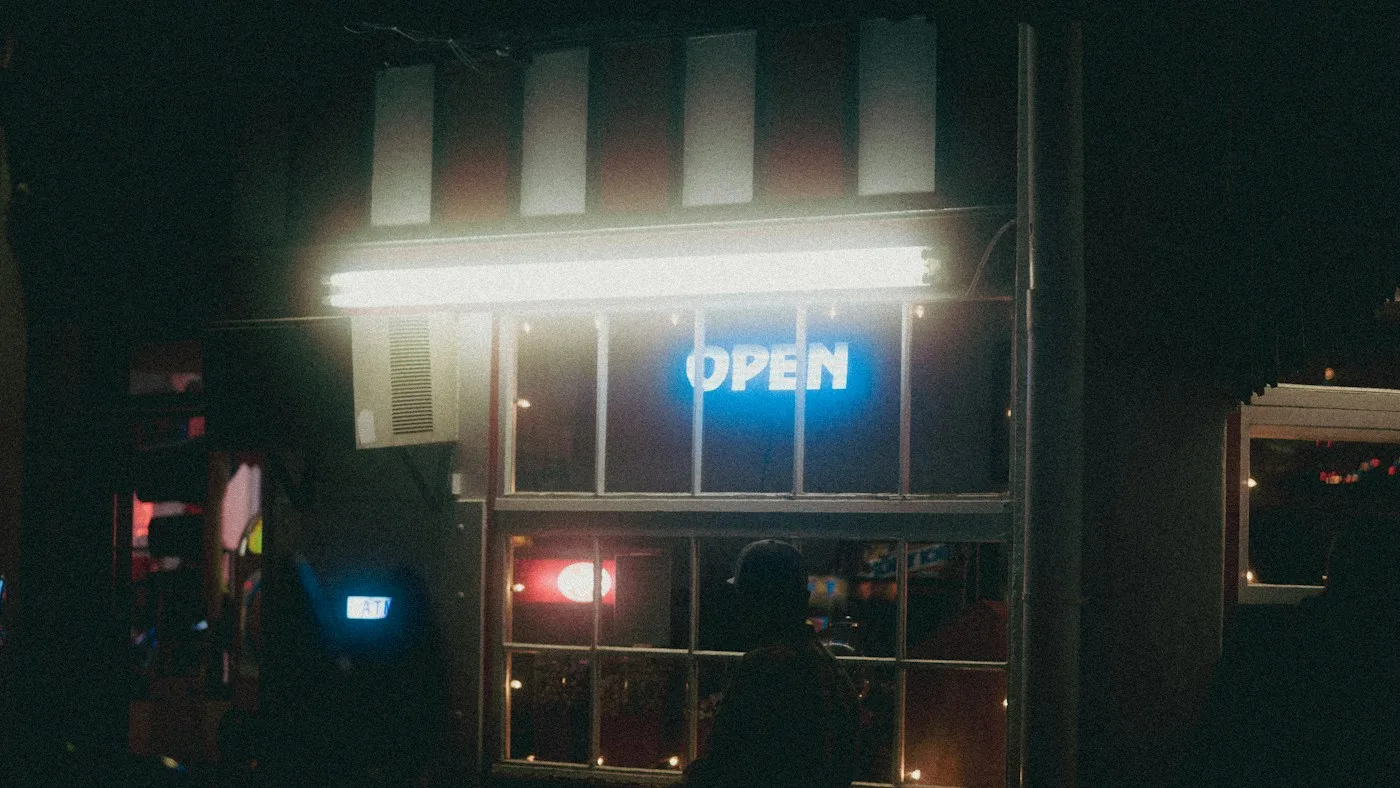 A small shop lit up at night with a blue neon open sign in the window